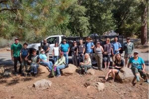 Volunteers in outdoor gear stand in front of a pickup truck with trees in the background, as they get ready to do a river cleanup along the Tuolumne River.